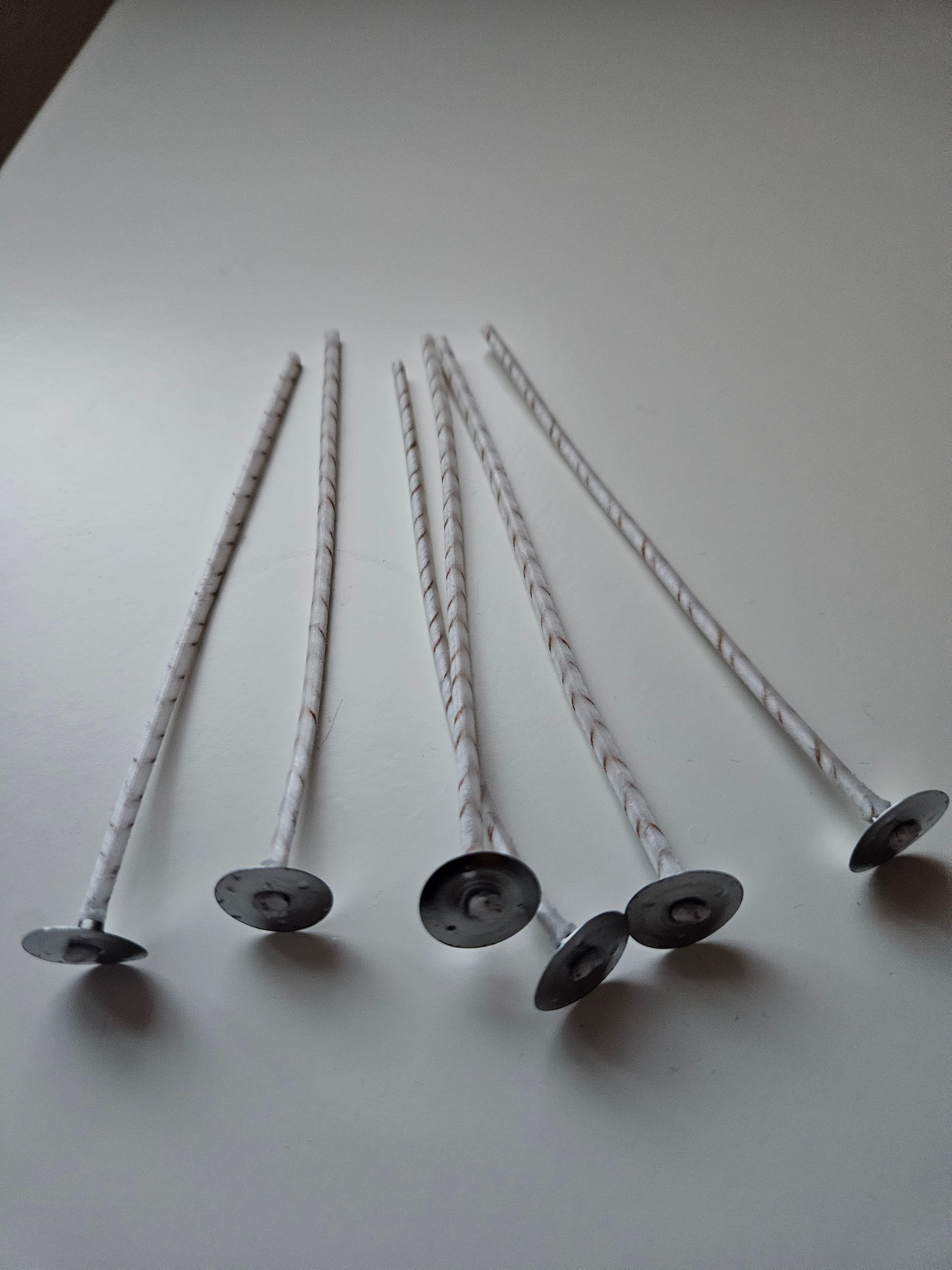 Sechs weiße Dochte mit Metallbasis für Kerzen auf weißem Untergrund