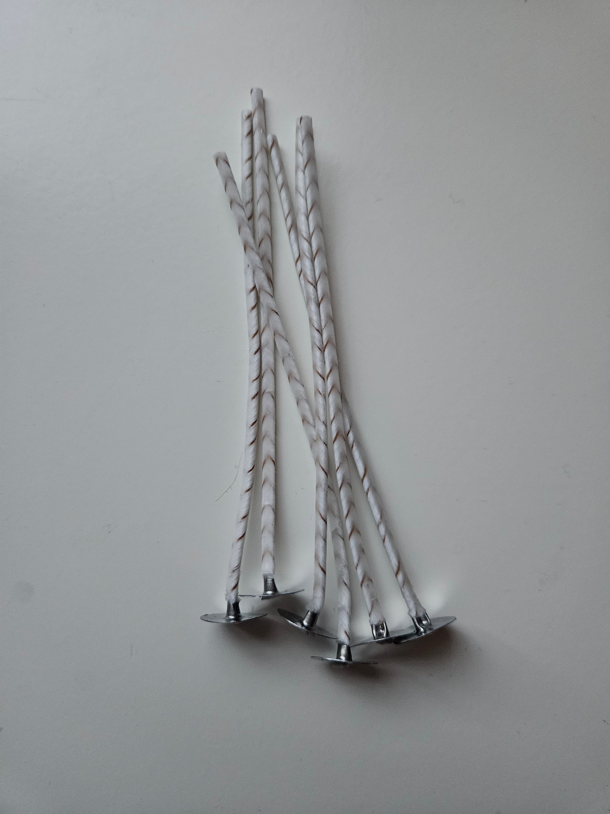 Sechs weiße Kerzendochte mit Metallplättchen auf grauem Hintergrund